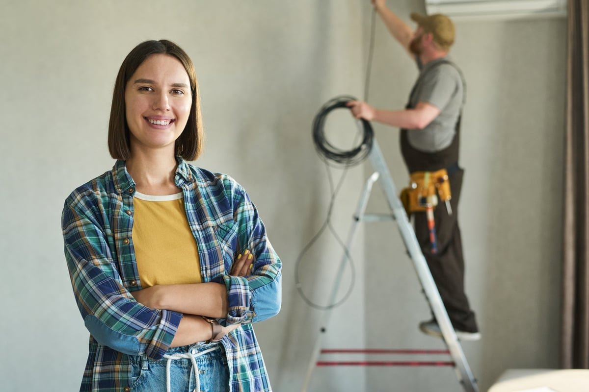 Homeowner smiling while a technician installs equipment in the background